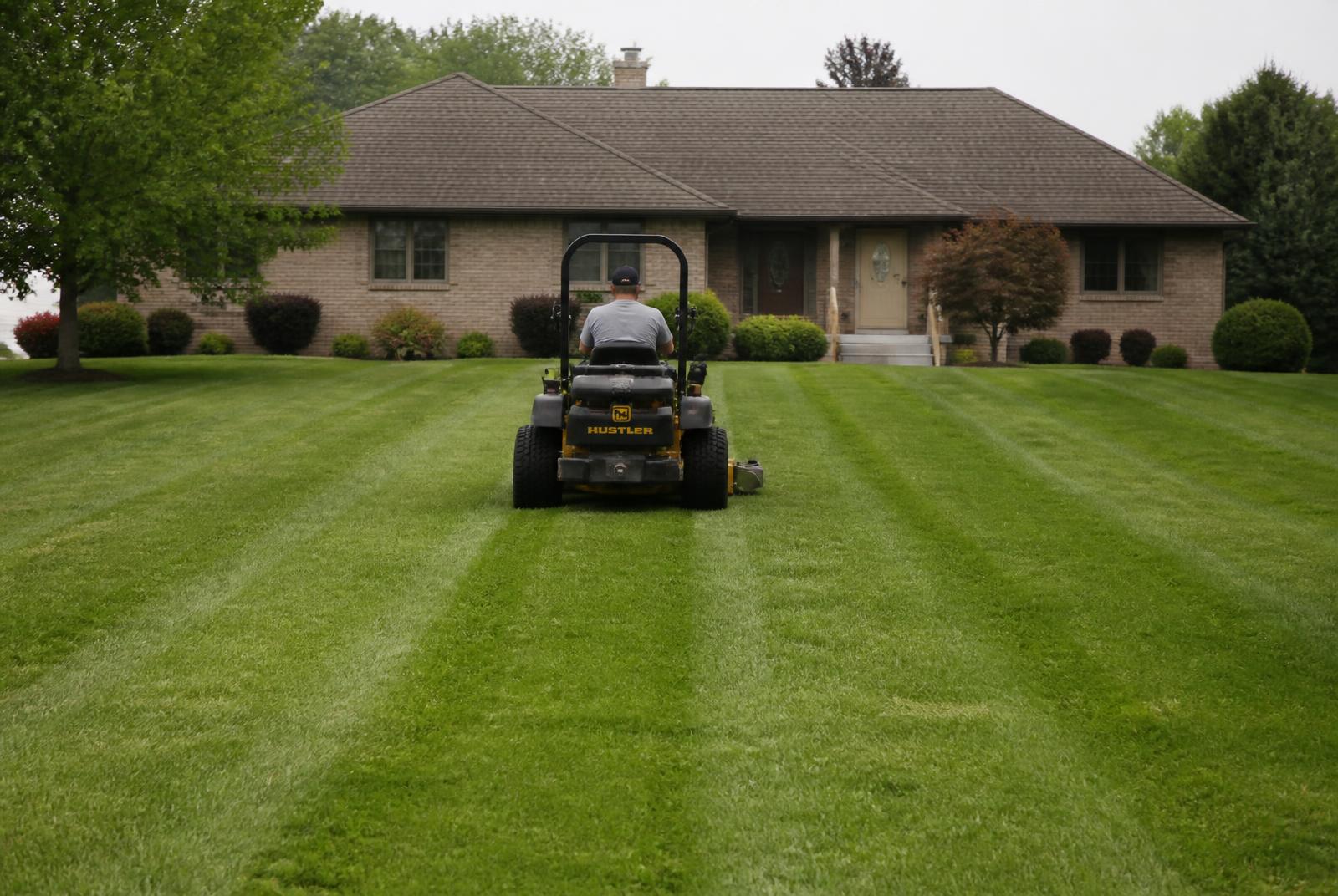 Zero-turn mower cutting stripes into a large green lawn