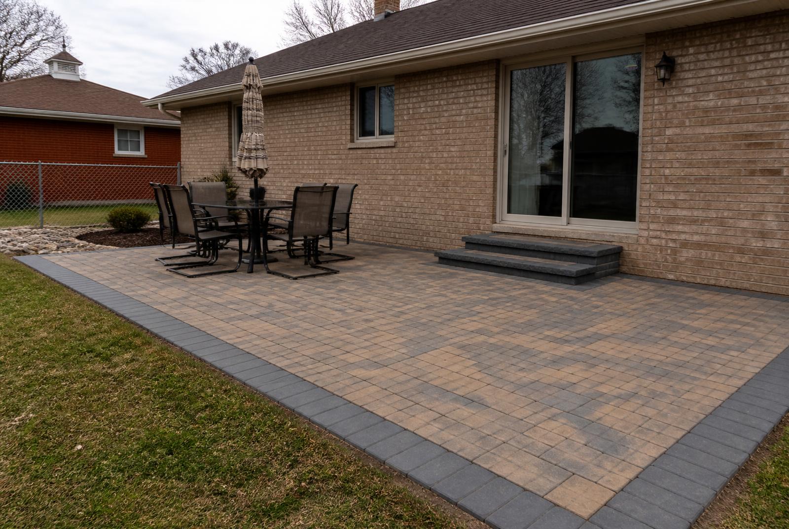 Newly installed paver patio with a charcoal border behind a brick Michigan home