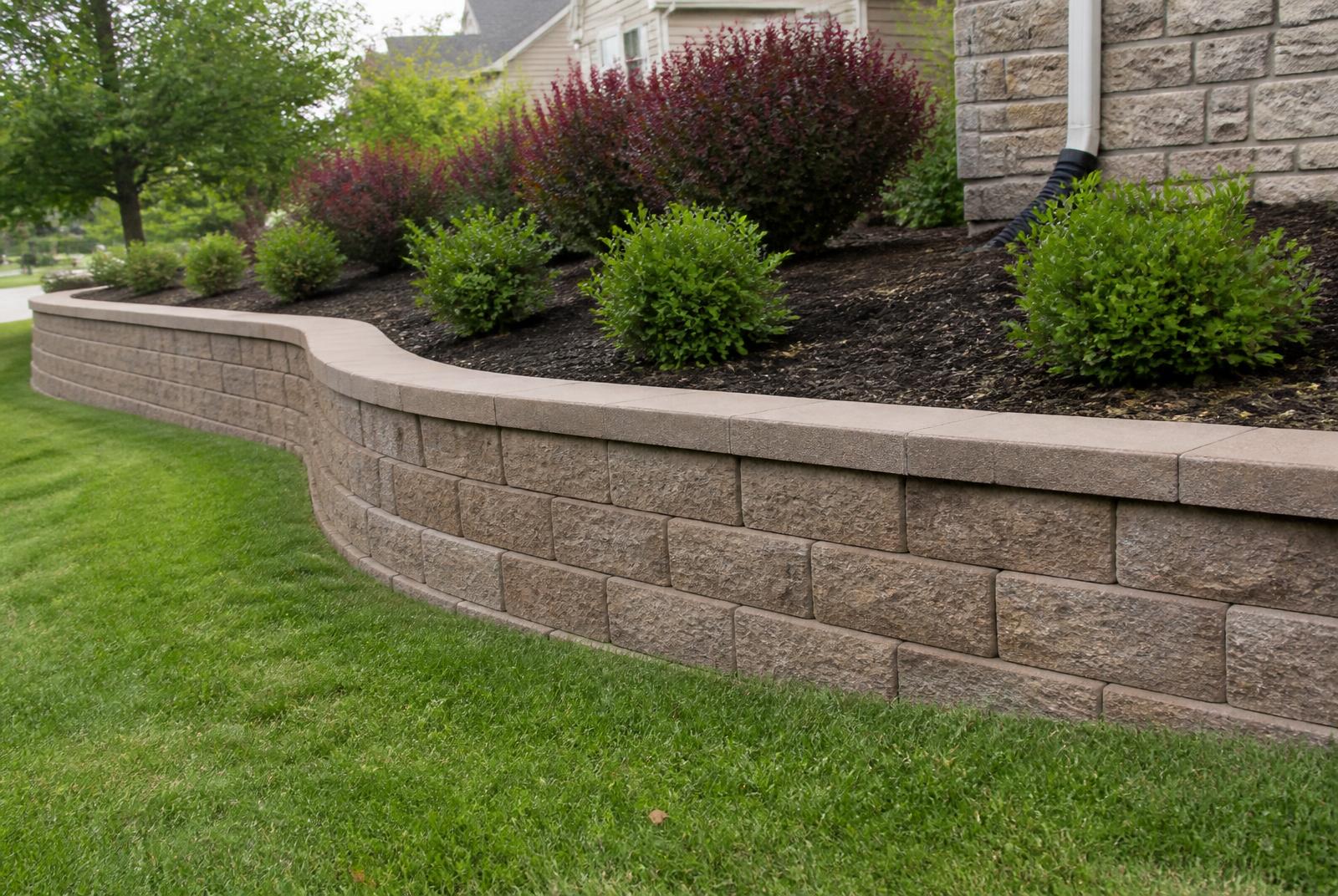 Curved block retaining wall with capstones supporting a mulched planting bed
