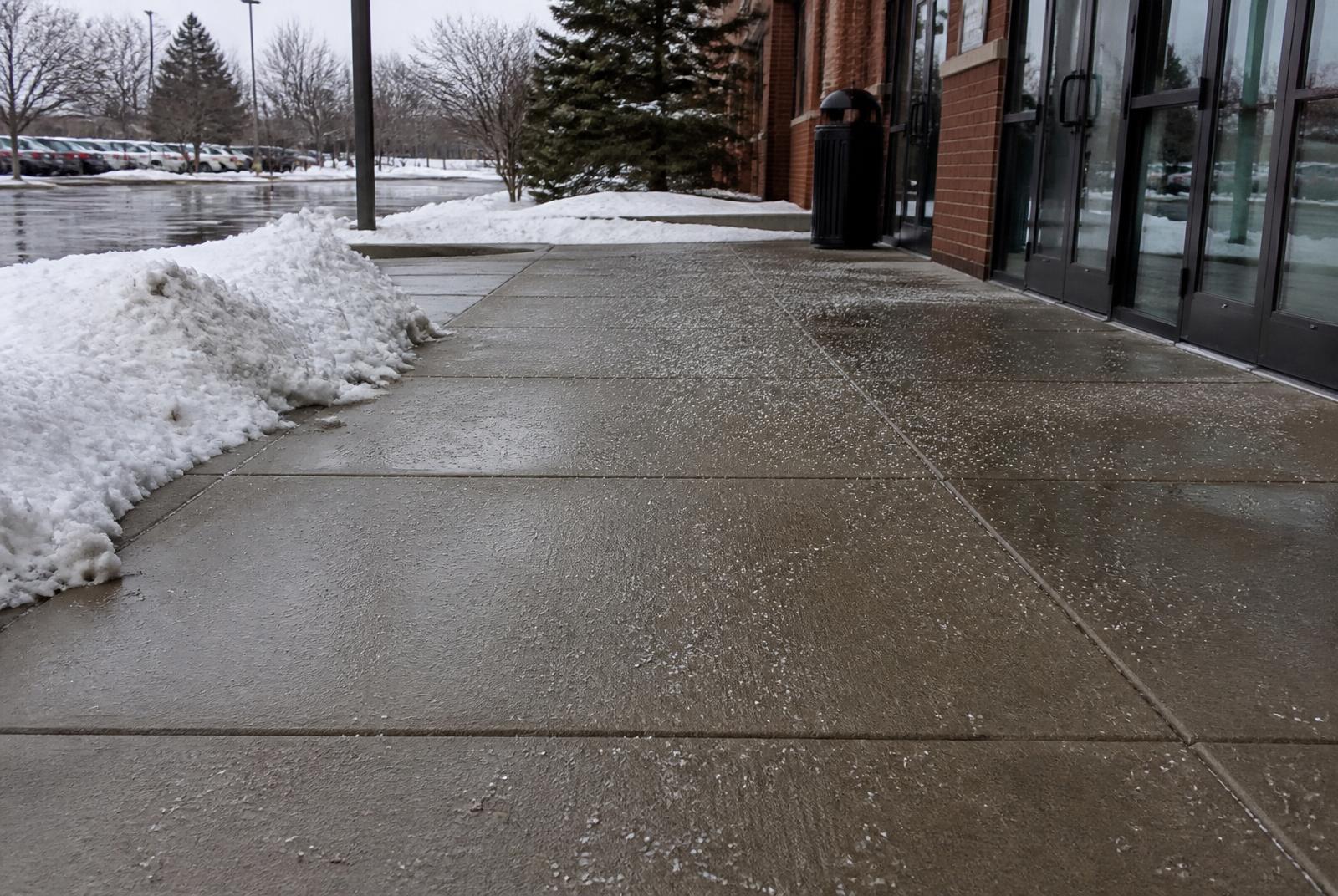 Salted and cleared commercial sidewalk with snowbanks piled at the curb